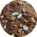 Mezcla de rooibos con trozos de manzana, pétalos de rosa y almendra laminada rosa, en primer plano.