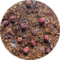Té rooibos con grosellas, frambuesas secas y pétalos de flores moradas sobre fondo de hojas secas marrones.