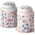 Latas metálicas decoradas con flores silvestres en tonos azules, rosas y naranjas, tapa blanca y rosa pastel.