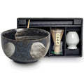 Set para matcha con bowl cerámico negro con detalles blancos, bate de bambú y recipiente blanco en estuche negro.