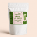 Bolsa blanca mate de 100g con etiqueta verde de Matcha Chai Latte y vaso con bebida verde al lado.