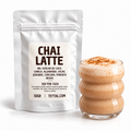Bolsa blanca de chai latte en polvo junto a un vaso de vidrio con bebida cremosa y espuma.